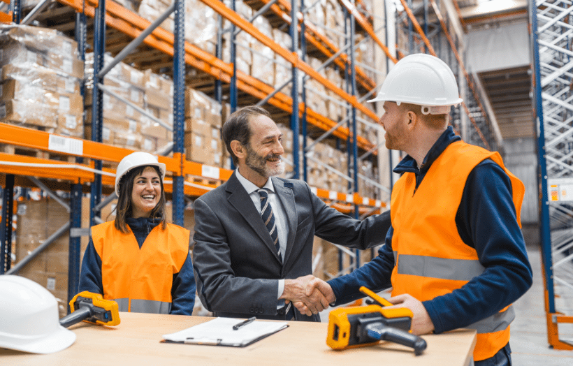 Business professional shaking hands with warehouse worker in a fulfillment center.