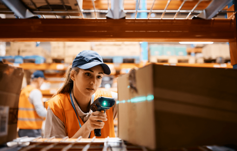 Fulfillment center associate scanning a barcode on a cardboard box using a handheld scanner in a warehouse