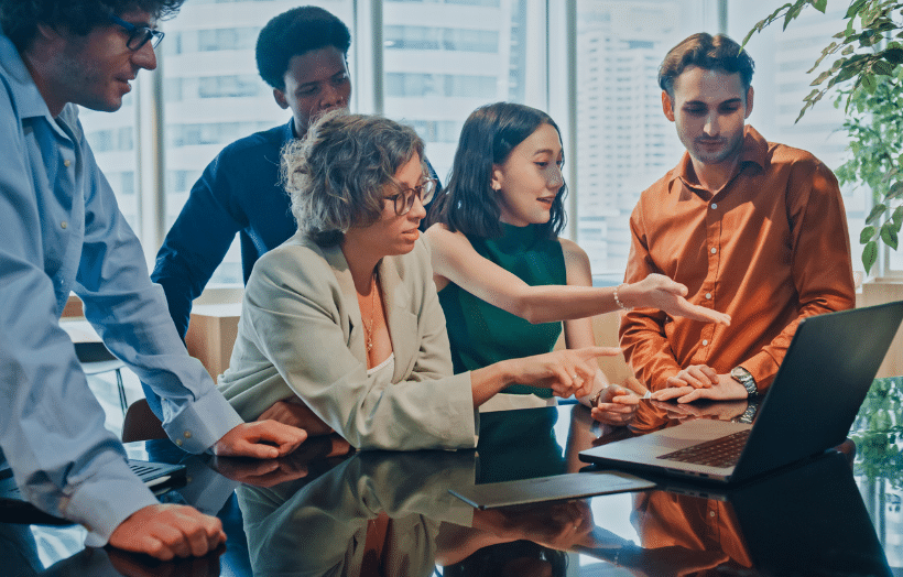 Diverse business team collaborating around laptop in modern office conference room