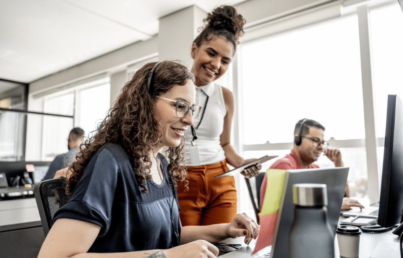 Contact center supervisor coaching associate at computer while team works in background