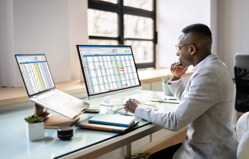 Business professional analyzing sales data across dual monitors in a modern office.