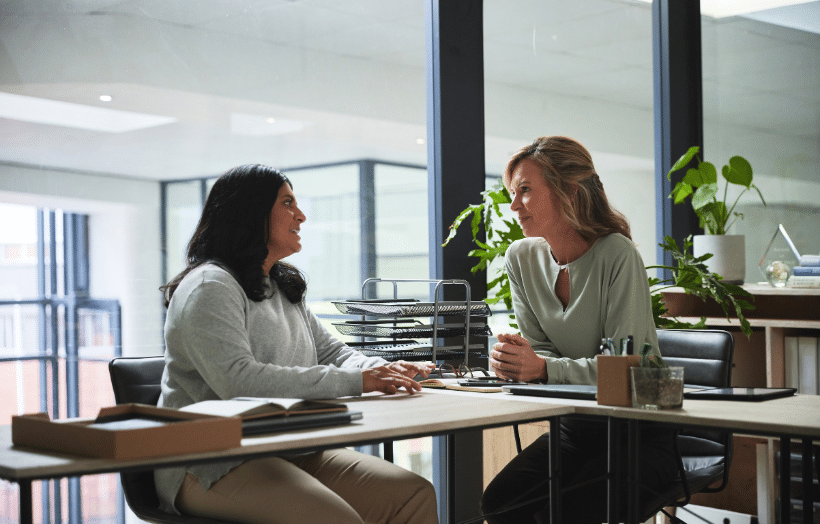 Two colleagues in a supportive one-on-one conversation at an office desk